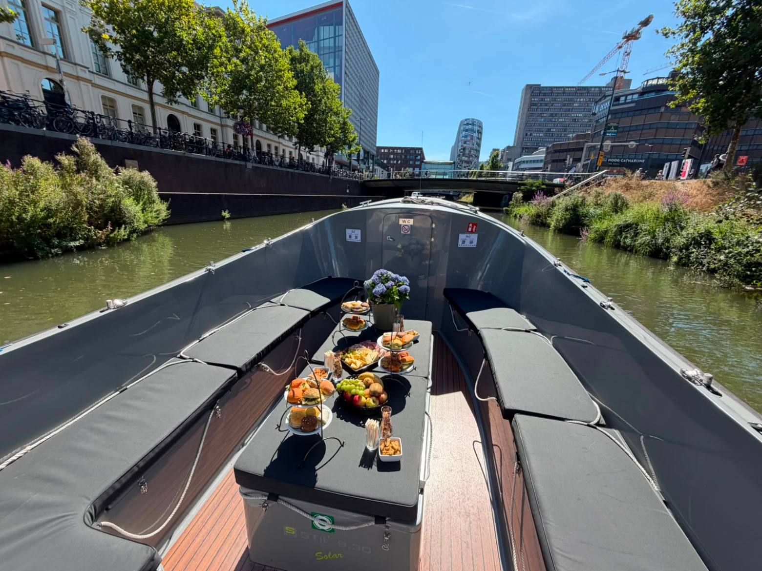 Open boat with food on table, urban canal setting, sunny day.