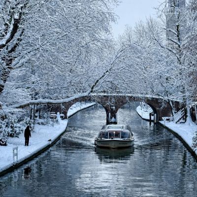 Boat on snowy canal under bridge with snow-covered trees.