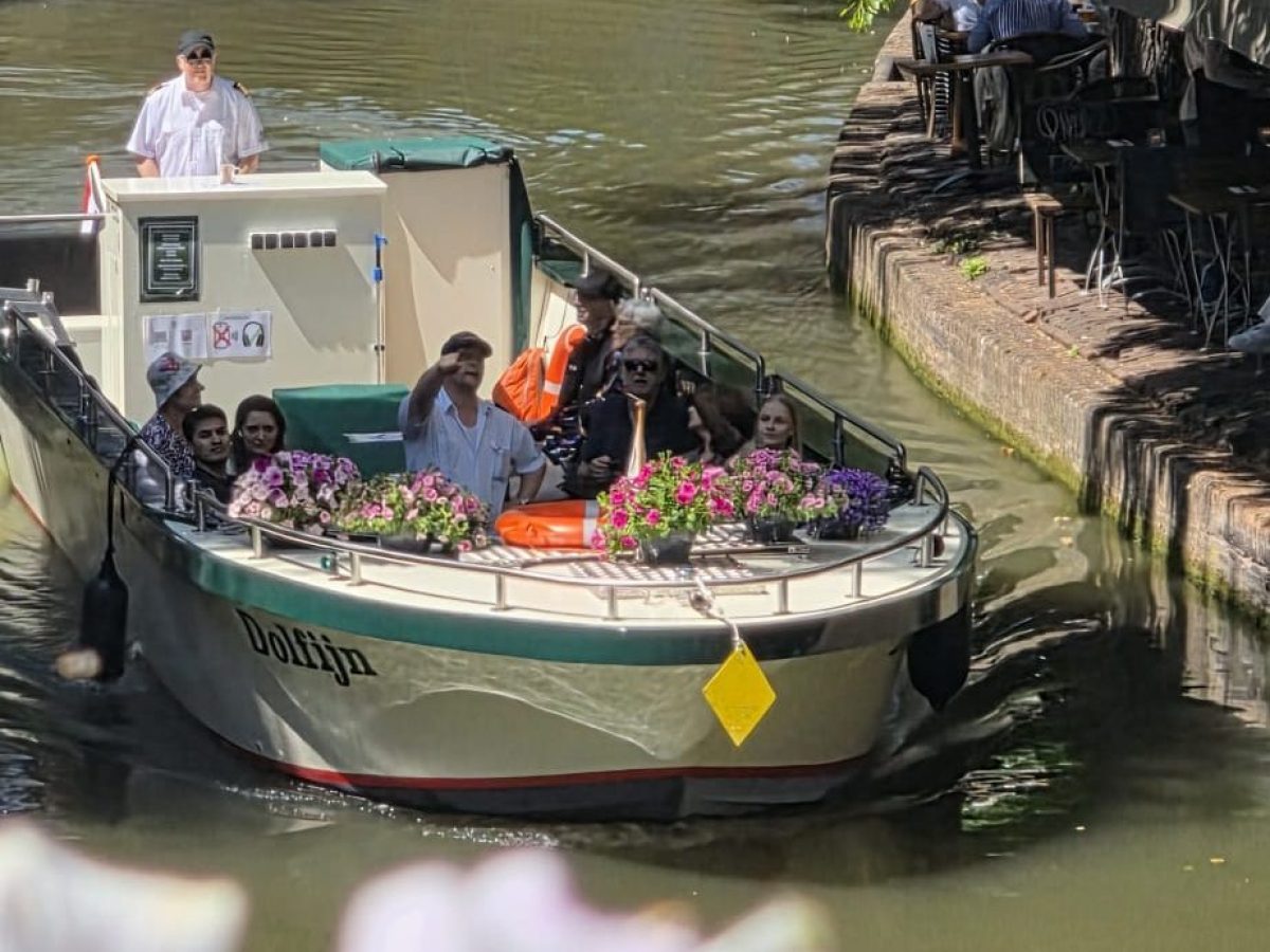 Boat with people passing under a bridge on a sunny canal.