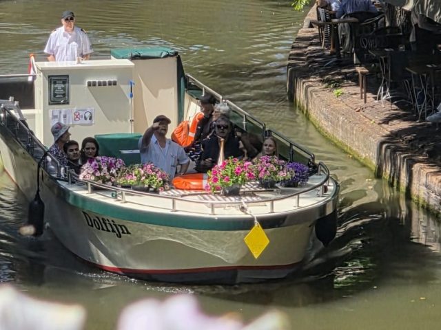 Boat with people passing under a bridge on a sunny canal.