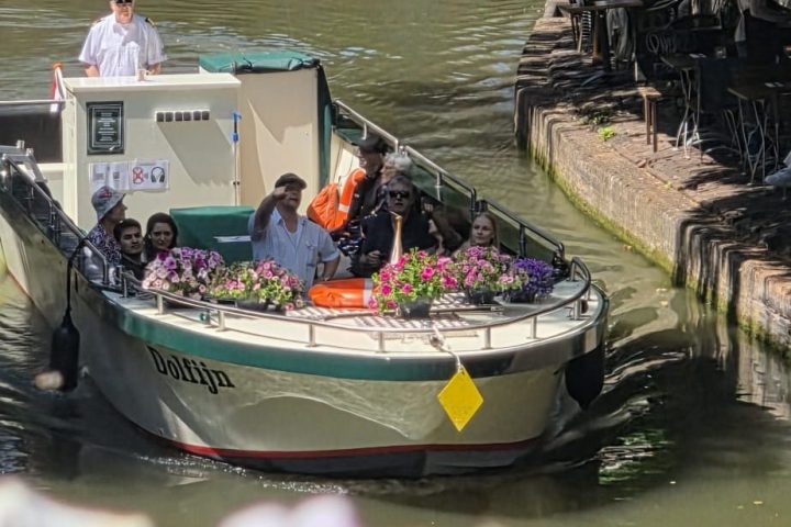 Boat with people passing under a bridge on a sunny canal.