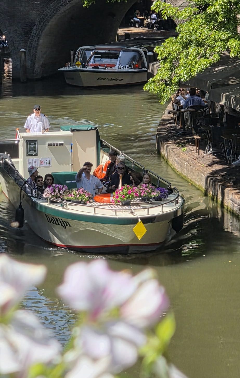 Boat with people passing under a bridge on a sunny canal.