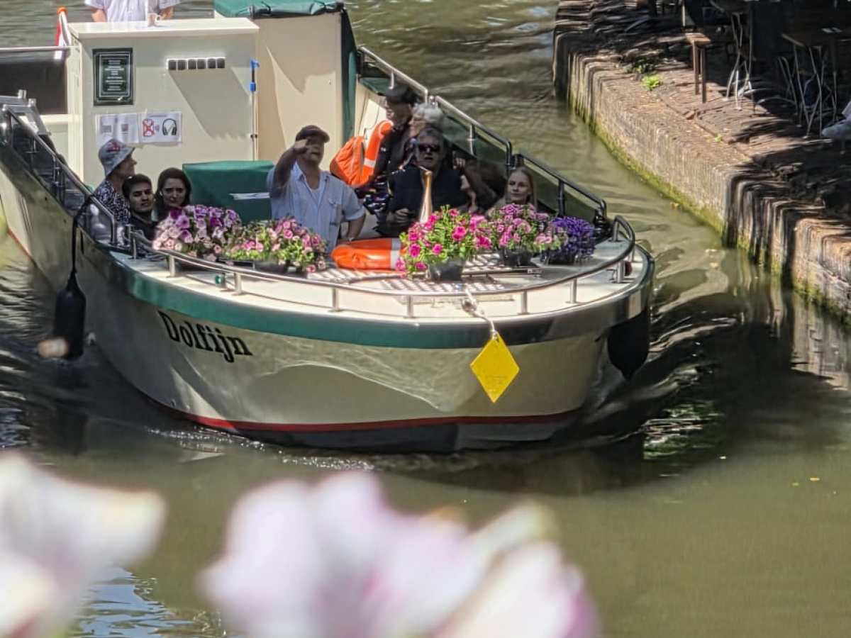 Boat with people passing under a bridge on a sunny canal.