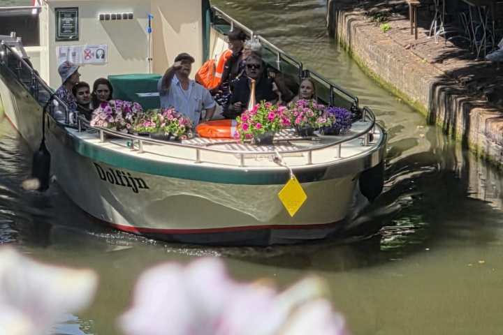 Boat with people passing under a bridge on a sunny canal.
