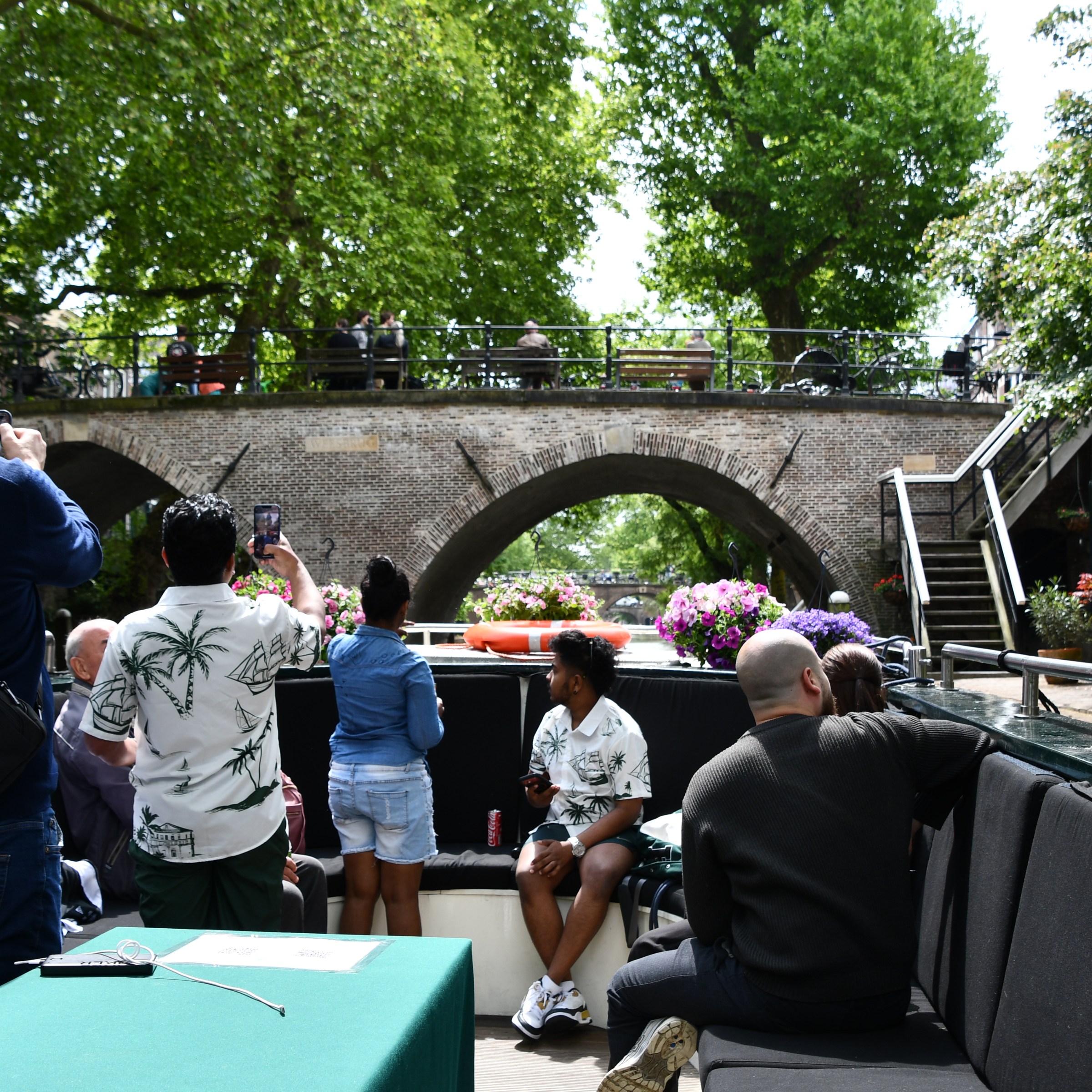 People on a boat tour photographing a scenic stone bridge surrounded by trees.