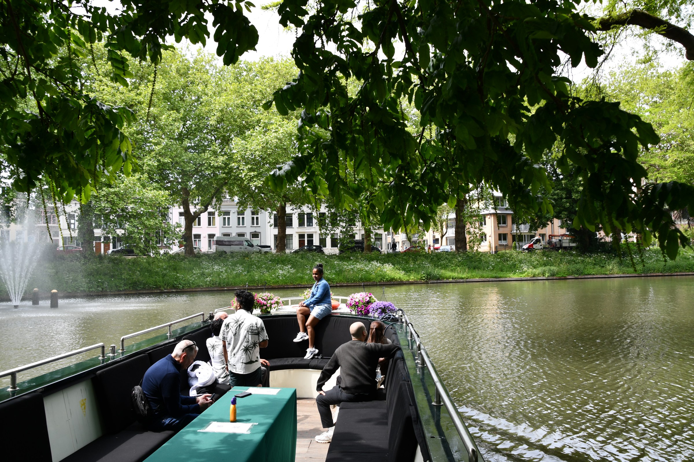 People sitting on a boat in a park with trees and a pond.
