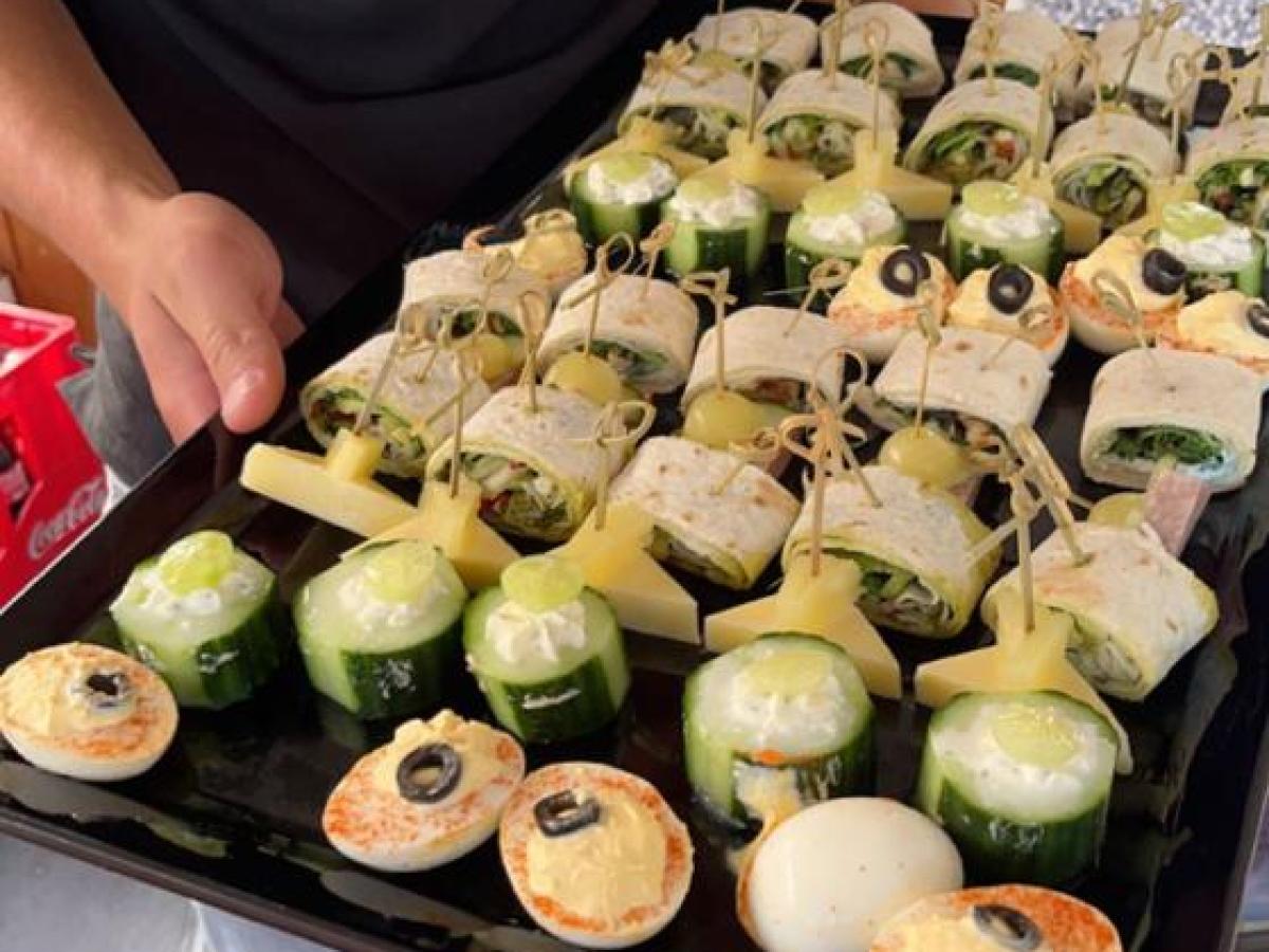 Person holding a tray with assorted appetizers, including rolls and cucumber bites.