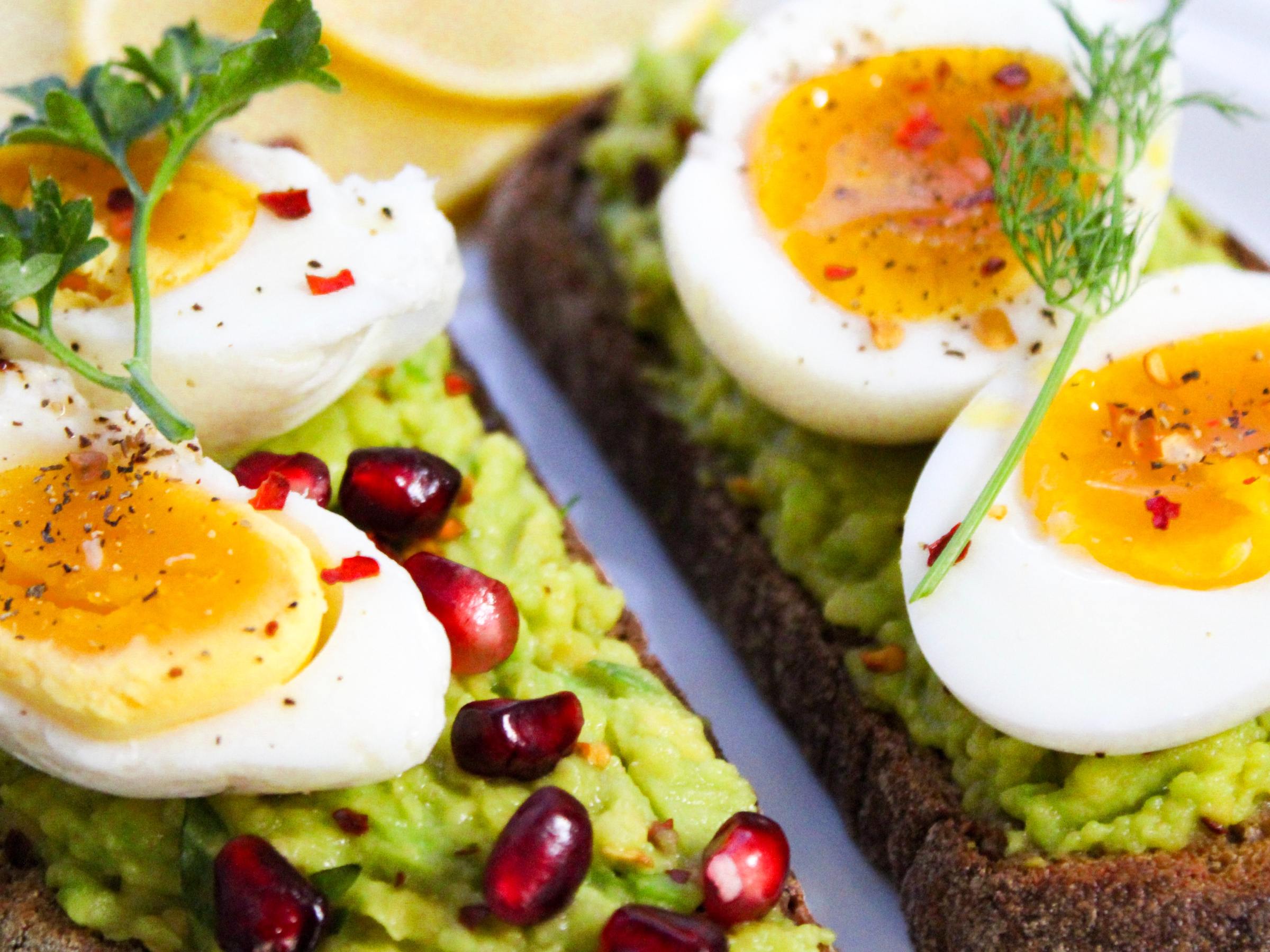 Avocado toast with sliced boiled eggs, pomegranate seeds, and herbs on a plate.