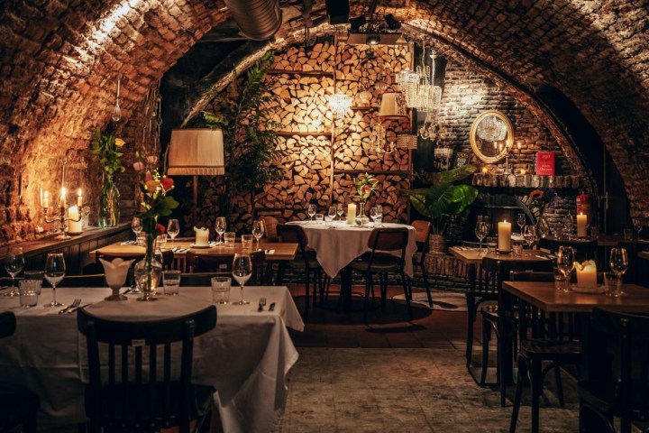 Cozy restaurant with arched brick ceiling, candle-lit tables, and a wood stack backdrop.