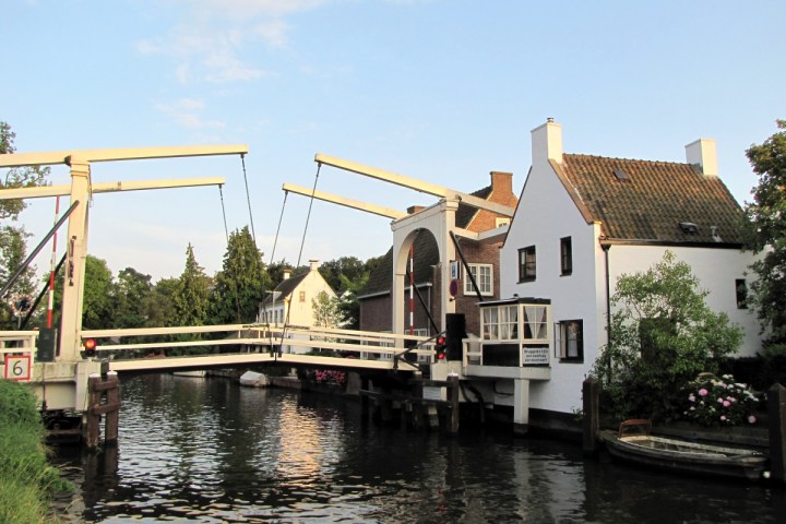 Dutch canal with a white drawbridge and traditional houses at sunset.