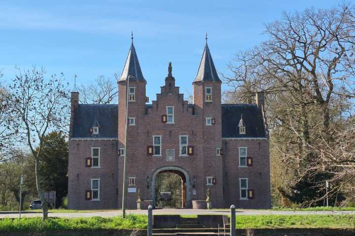 Historic brick castle with two towers and arched entrance, surrounded by bare trees.