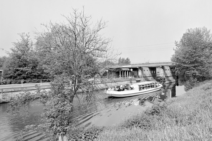 Boat on a canal near a bridge and trees in grayscale.