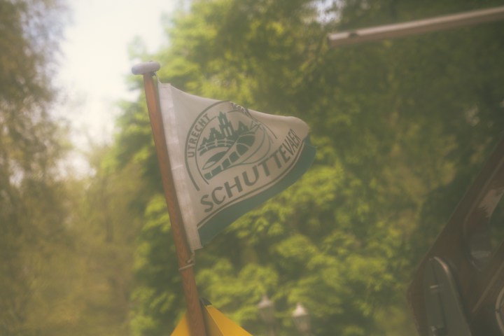 Blurred image of a flag on a boat with trees in the background.