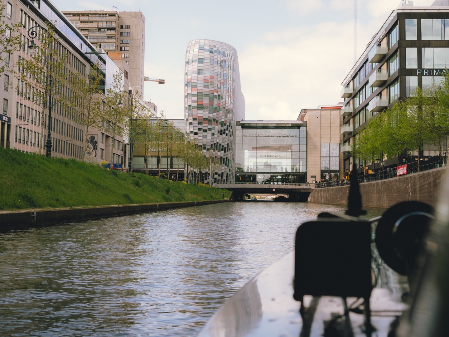 Modern buildings and canal view from a boat under a bridge.