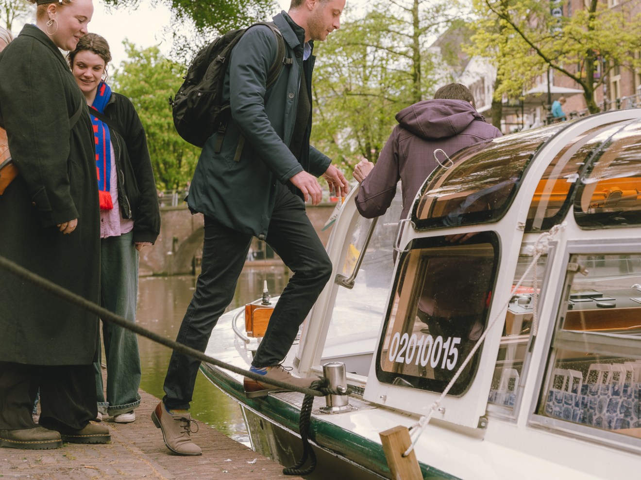 People boarding a canal boat in a leafy area with cobblestone path.