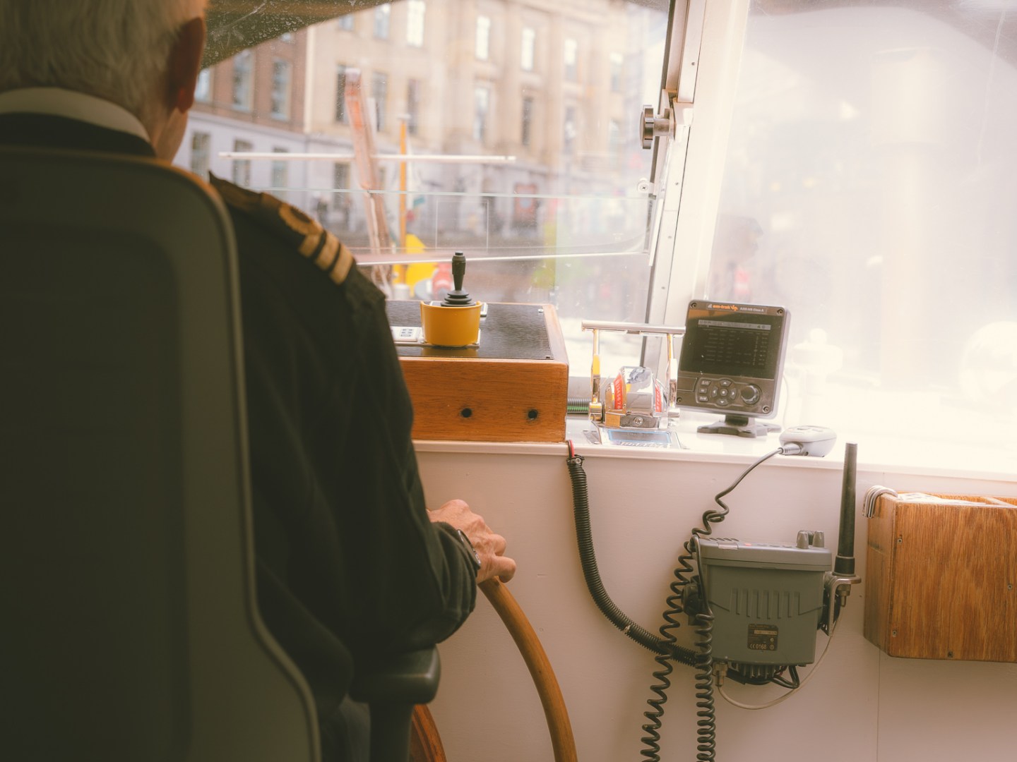 Boat captain steering with city view through window.