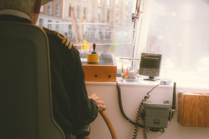 Boat captain steering with city view through window.