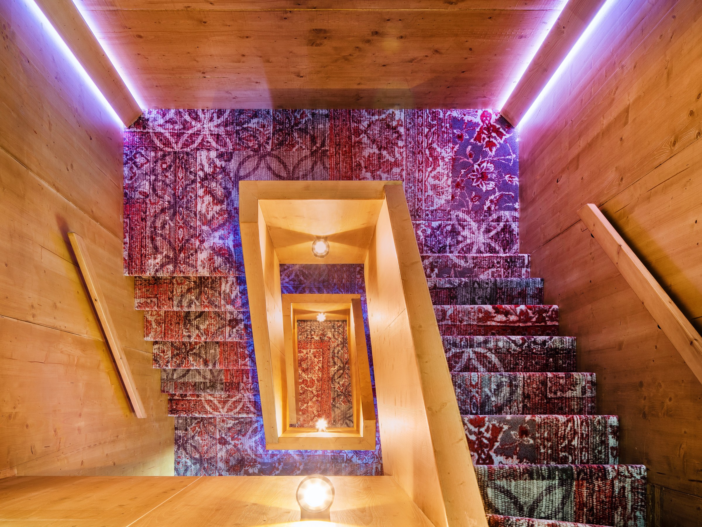 Wooden staircase with vibrant patterned carpets, viewed from above.