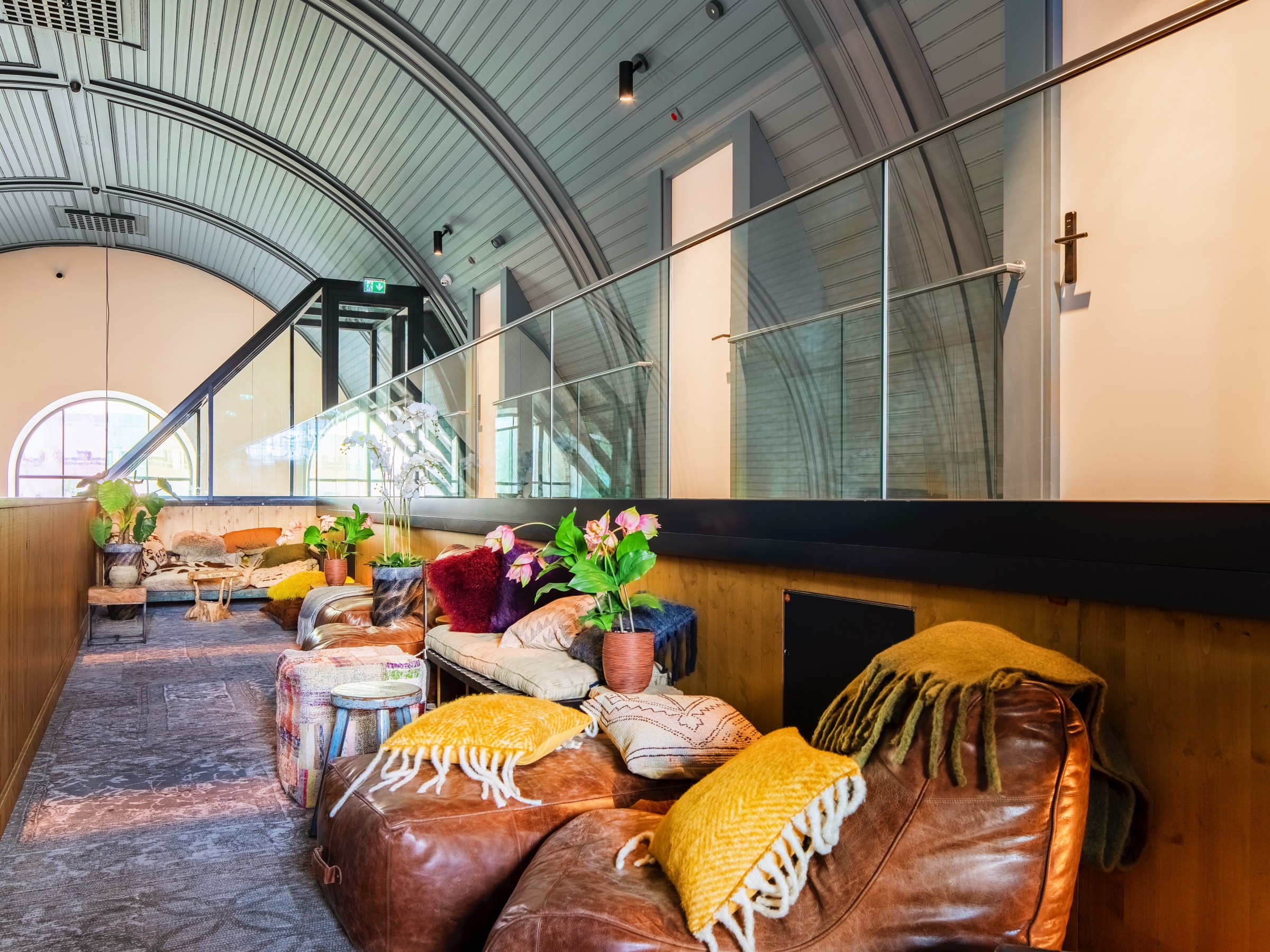 Cozy loft with leather chairs, cushions, and plants under an arched ceiling.
