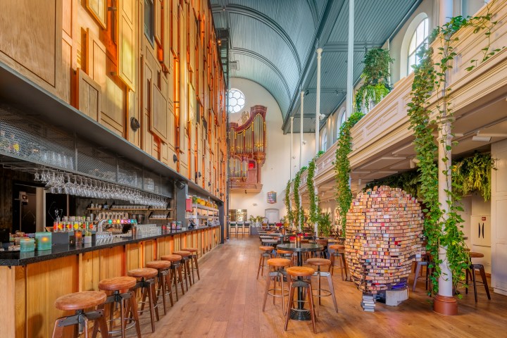 Spacious bar with high ceilings, stools, foliage, and organ pipes in a converted church.