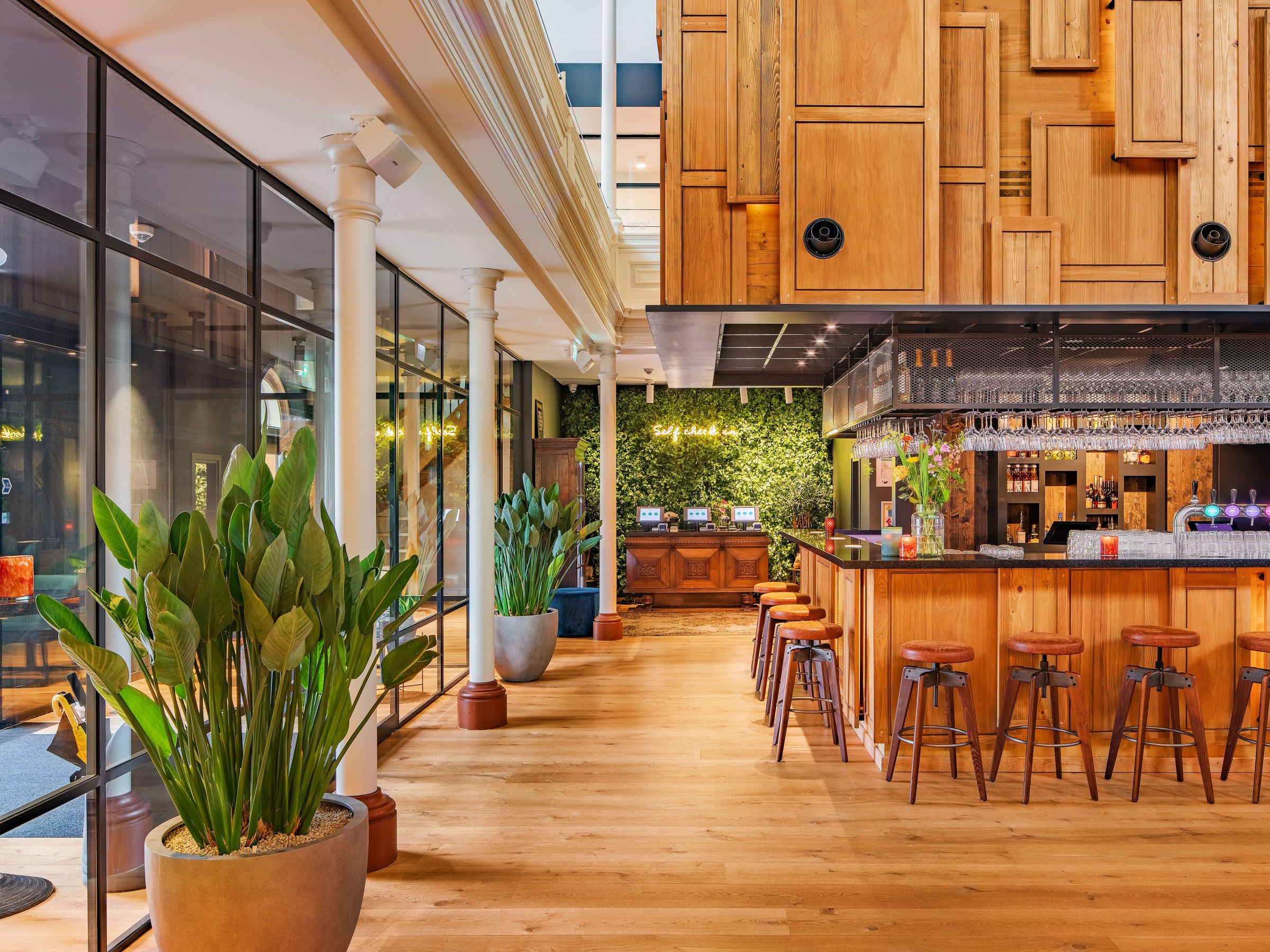 Modern bar with wooden decor, stools, and greenery on walls and in pots.