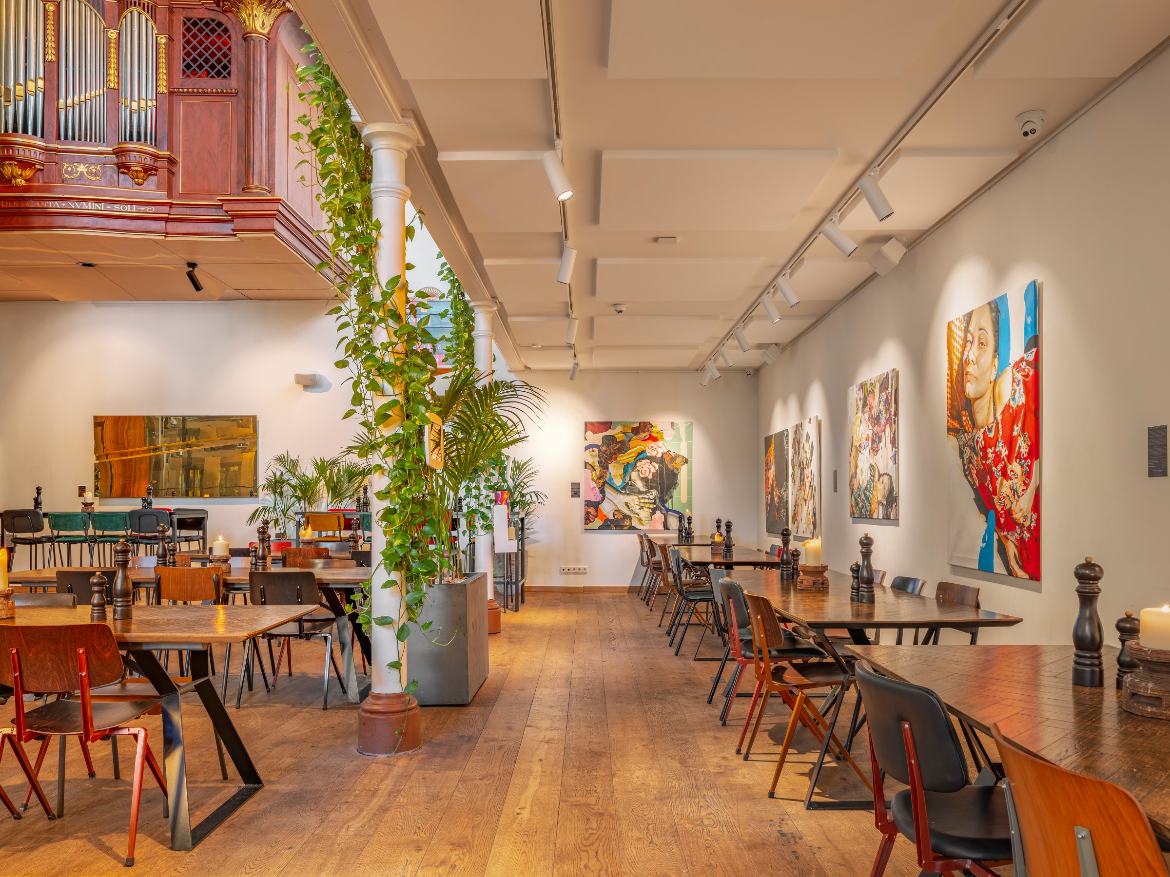 Spacious art gallery with tables, chairs, and vibrant paintings on walls.