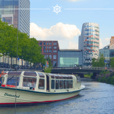 Boat navigating a city canal with modern buildings and greenery.