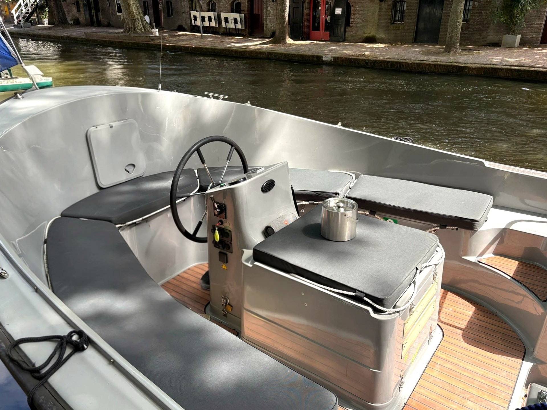 Small motorboat with gray seating and wooden floor on a canal.