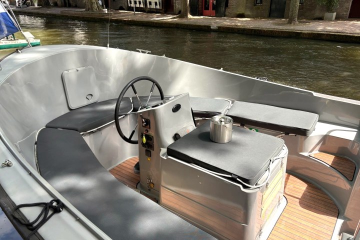 Small motorboat with gray seating and wooden floor on a canal.