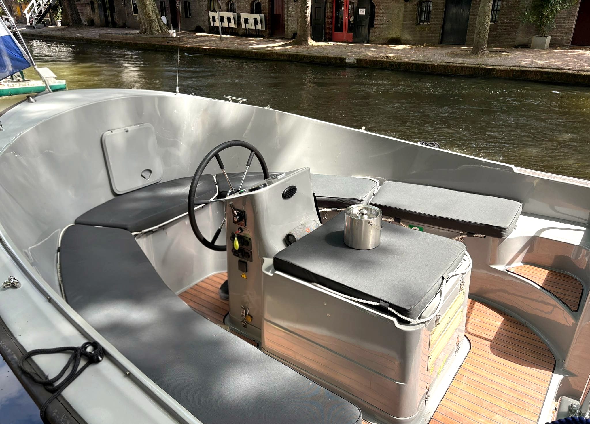 Small motorboat with gray seating and wooden floor on a canal.