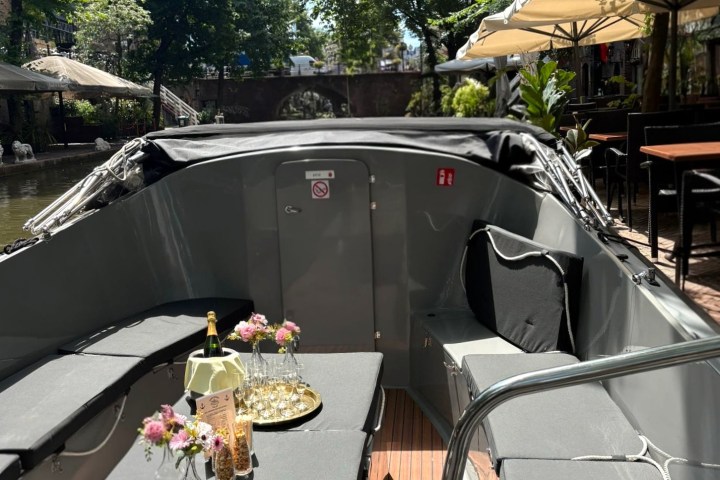 Cozy boat seating with flowers and drinks under sunny trees.