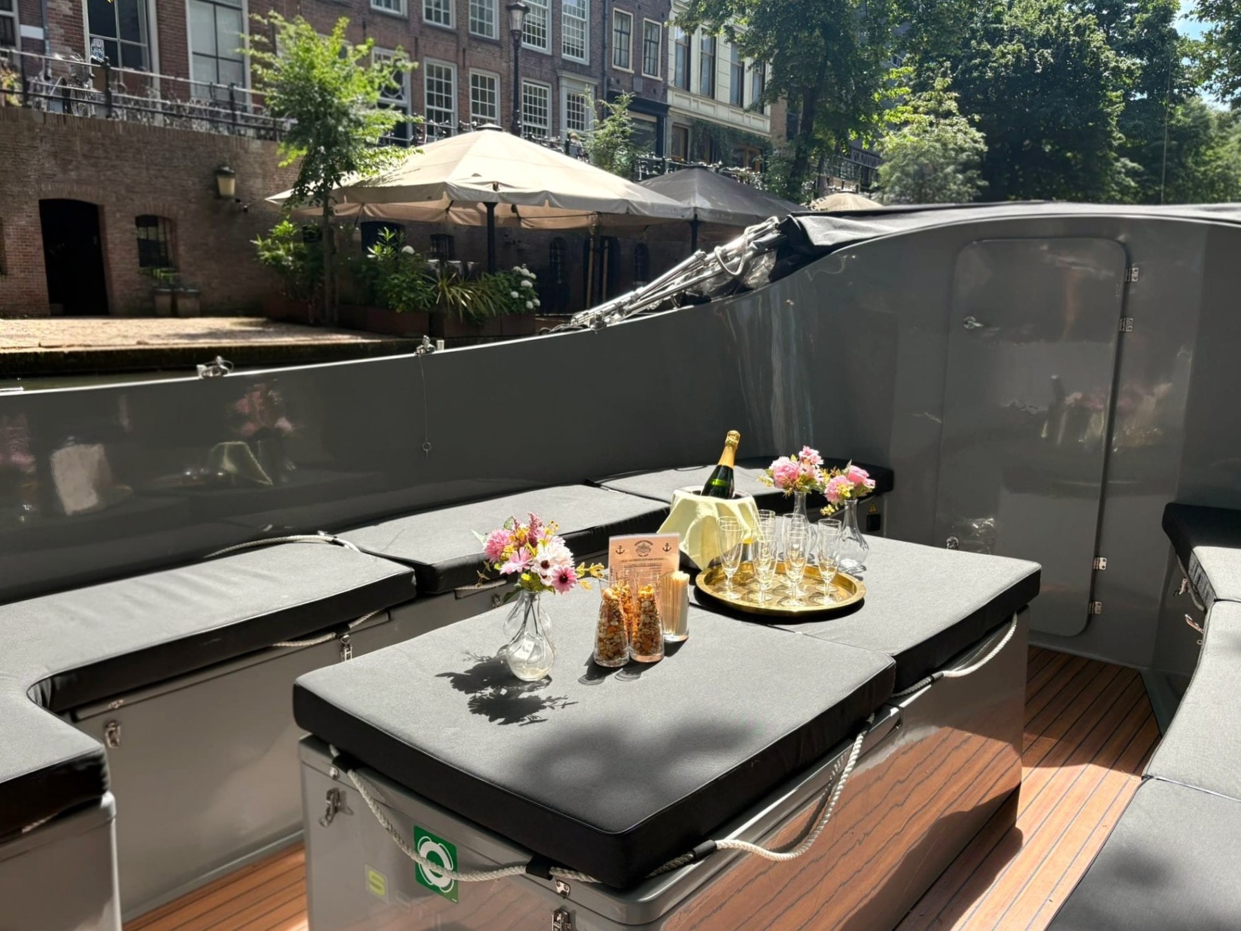 Boat with champagne, flowers, and glasses on a canal, under sunlight.