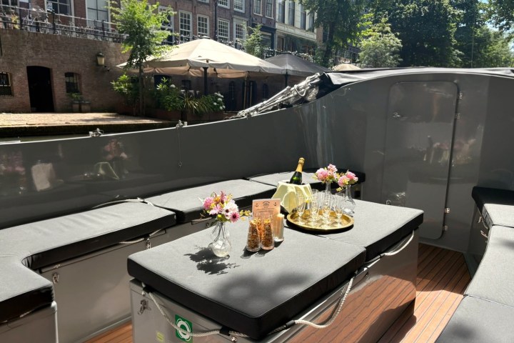 Boat with champagne, flowers, and glasses on a canal, under sunlight.