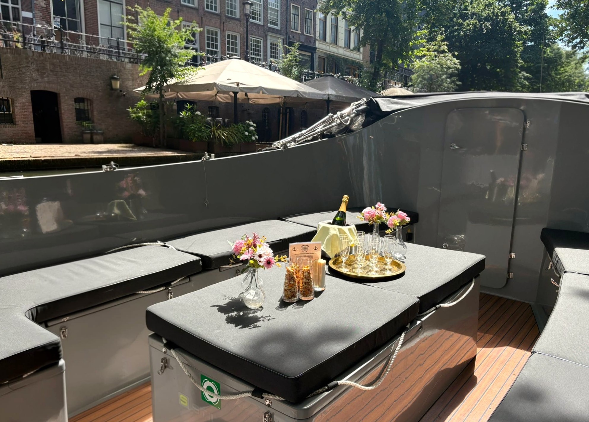 Boat with champagne, flowers, and glasses on a canal, under sunlight.