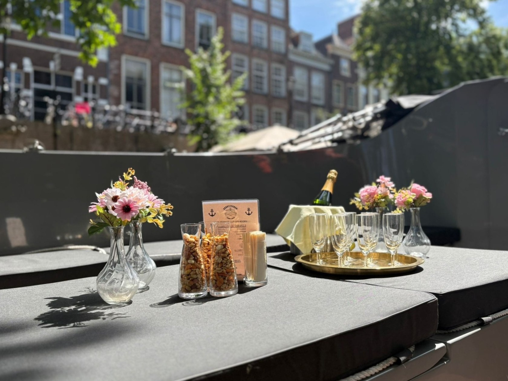 Outdoor table with flowers, snacks, glasses, and champagne under a sunny sky.