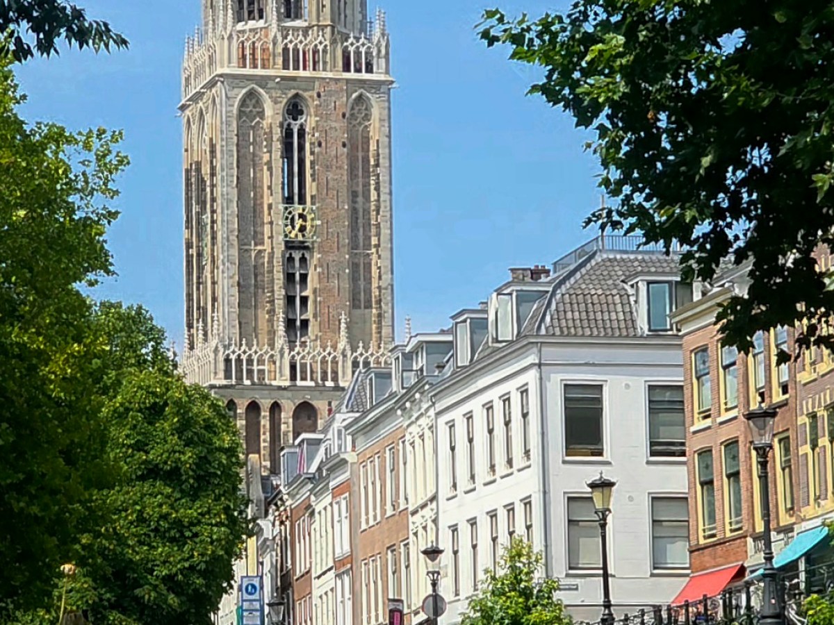 Historic tower and canal with boats and bridge in a scenic cityscape.